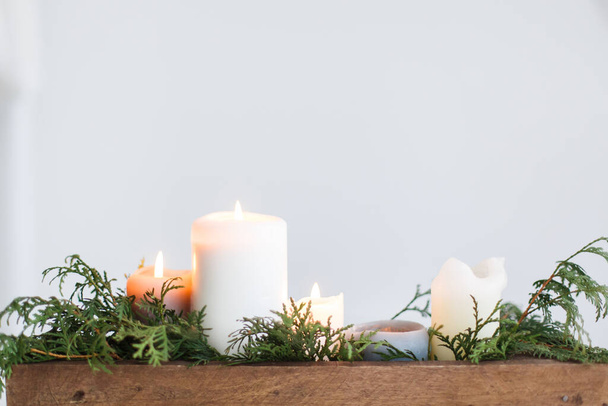 Burning candles in rustic wooden box with cedar branches on wooden table on white background. Festive christmas table decoration, winter holiday decor and wedding arrangement. Copy space - Foto, Bild