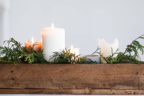 Brennende Kerzen in rustikaler Holzkiste mit Zedernzweigen auf Holztisch auf weißem Hintergrund. Festliche weihnachtliche Tischdekoration, winterliche Urlaubsdekoration und Hochzeitsarrangements. Kopierraum - Foto, Bild
