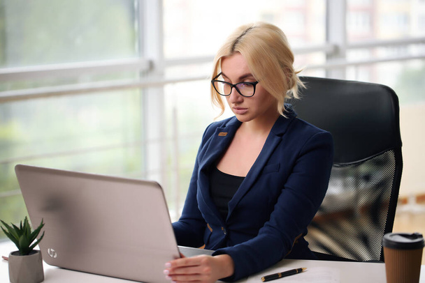 smiling blonde businesswoman with glasses using laptop in the office - Photo, Image