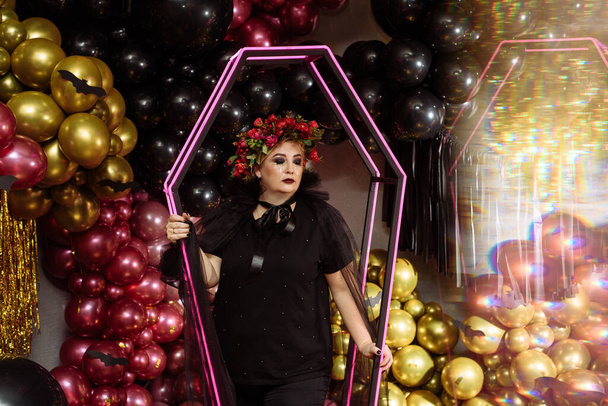 Krásná dospělá žena v černém halloween kostýmu na pozadí balónů a dekorací. Čarodějnice s černým kouřem a jiskřícími tvářemi - Fotografie, Obrázek