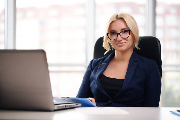 smiling blonde businesswoman with glasses using laptop in the office - Photo, image