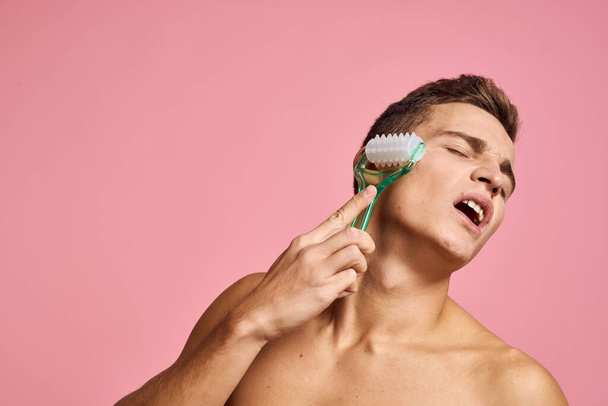 Handsome man with massager in hand on isolated pink background cropped view clean skin - Photo, Image
