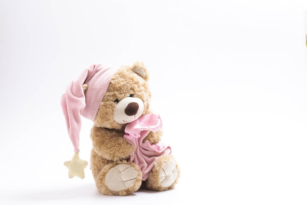 Sleepy soft toy bear in a cap with a pink blanket on a white background. The concept of childhood, sleep, falling asleep, dreams. Isolated. Horizontal. - Photo, Image