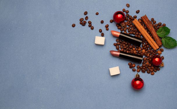 Christmas card. Lipstick Nude shades lies in coffee beans with cinnamon, mint and sugar on a blue background.Space for the text. - Foto, Imagem