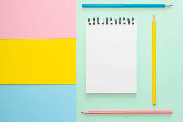 多色紙に白いシートと色鉛筆でスパイラルノート。オフィス、学校、創造性、学習の概念。平面、コピースペース、ミニマリズム。ピンク、青、黄色の色合い. - 写真・画像