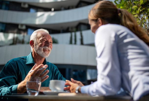 Счастливый зрелый мужчина сидит кафе с молодой деловой женщиной и болтает - Фото, изображение