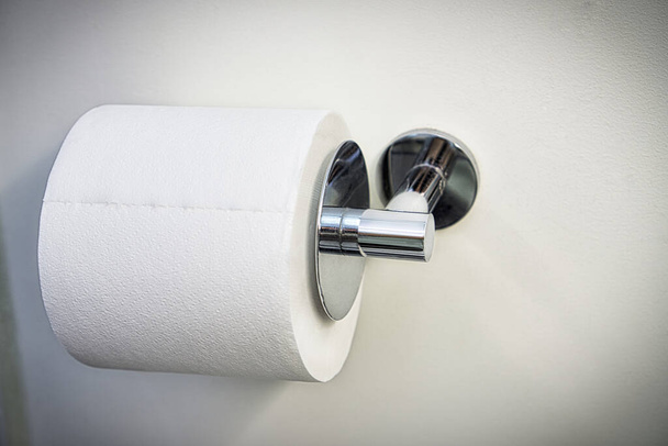 A white roll of toilet paper hanging on a chrome holder on a bathroom wall. - Photo, Image