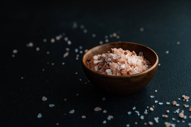 Zdravá koncepce vaření s dřevěnou mísou plnou růžové hymayské soli na tmavém kamenném pozadí s kopírovacím prostorem - Fotografie, Obrázek