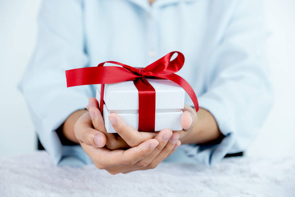Женщина в синей рубашке с белой подарочной коробкой, связанной красной лентой, на праздник подарков, таких как Рождество, День Святого Валентина. - Фото, изображение