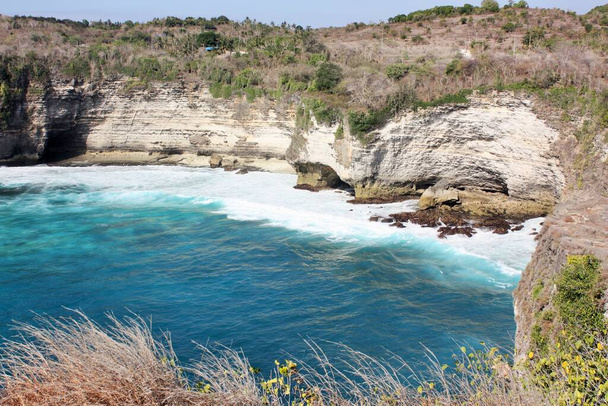 Хвилі розбиваються об скелястий берег на дні крутих скель (Нуса Пеніда, Індонезія). - Фото, зображення