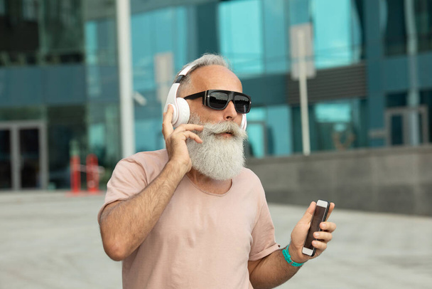 Hipster mature man listening to music via smartphone walking in the city - Photo, image