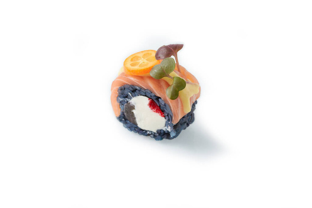 Roru oscuro - anguila ahumada, queso crema, aguacate, masago, semillas de sésamo, tempura, salsa picante en un plato blanco - Foto, imagen