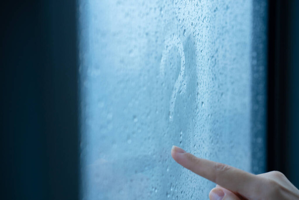 Female hand draws a question mark on a foggy window during the rain. A glass in drops of water - Φωτογραφία, εικόνα