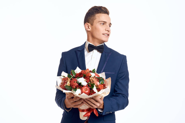 Elegancki mężczyzna w klasycznym garniturze z muszką trzyma w ręku bukiet kwiatów  - Zdjęcie, obraz