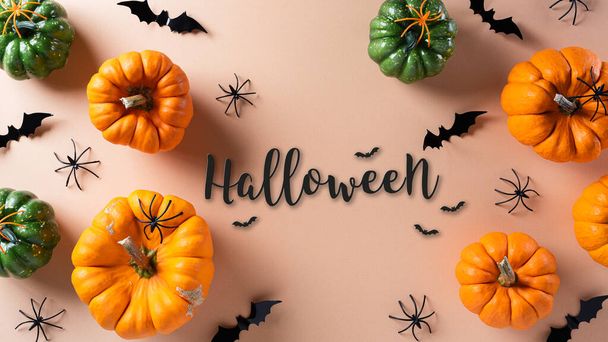 Απόκριες διακοσμήσεις από κολοκύθα και μαύρη αράχνη σε παστέλ πορτοκαλί φόντο. Επίπεδη lay, κορυφαία προβολή με Happy Halloween κείμενο. - Φωτογραφία, εικόνα