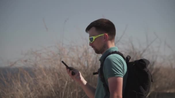 Caucasian man walks along trail on hill along sea, one-day hiker uses the Internet and smartphone app to navigate. Male builds a route in phone using satellites gps for orientation and geolocation - Footage, Video