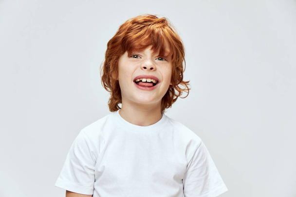 κοκκινομάλλα αγόρι δείχνει γλώσσα πρόσωπο κοντά crop view λευκό t-shirt  - Φωτογραφία, εικόνα