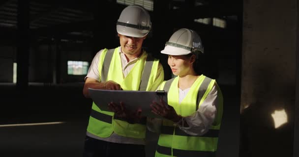 Ázsiai ipari mérnökök keménykalapban Biztonsági dzsekit viselnek, együtt dolgoznak az építési területen. - Felvétel, videó