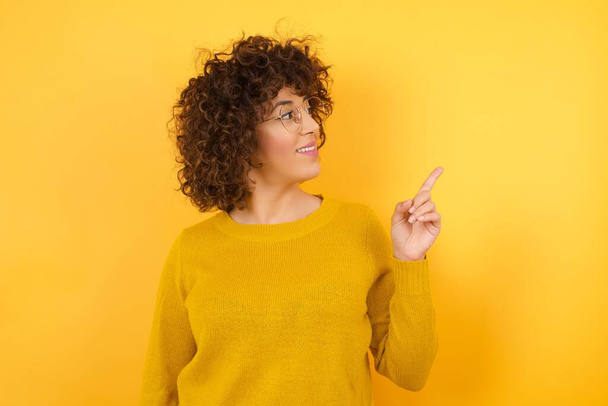 Smiling woman pointing finger on yellow wall  - Photo, Image