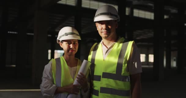 Πορτρέτο Ασίας βιομηχανικοί μηχανικοί σε σκληρό καπέλο φορώντας σακάκι ασφαλείας εργάζονται στο εργοτάξιο του κτιρίου μαζί - Πλάνα, βίντεο
