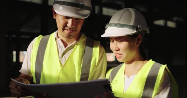 Ασιάτες βιομηχανικοί μηχανικοί στο σκληρό καπέλο φορώντας σακάκι ασφαλείας που εργάζονται στο εργοτάξιο του κτιρίου μαζί - Πλάνα, βίντεο