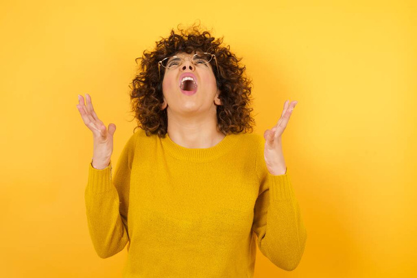shouting woman with curly hair in yellow studio, aggressive emotion - Photo, Image