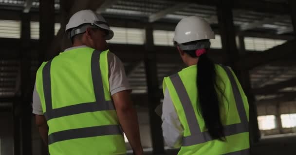 Sert Şapkalı Asyalı Endüstriyel Mühendisler. İnşaat alanında birlikte çalışan güvenlik ceketi giyiyorlar. - Video, Çekim