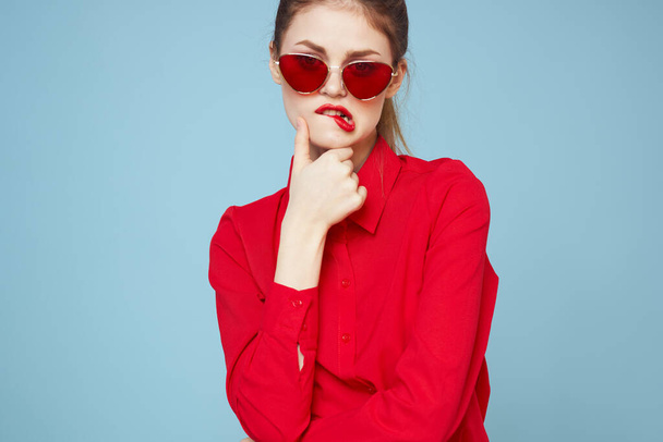 Beautiful woman in dark glasses red shirt bright makeup emotions attractive look blue background - Photo, Image