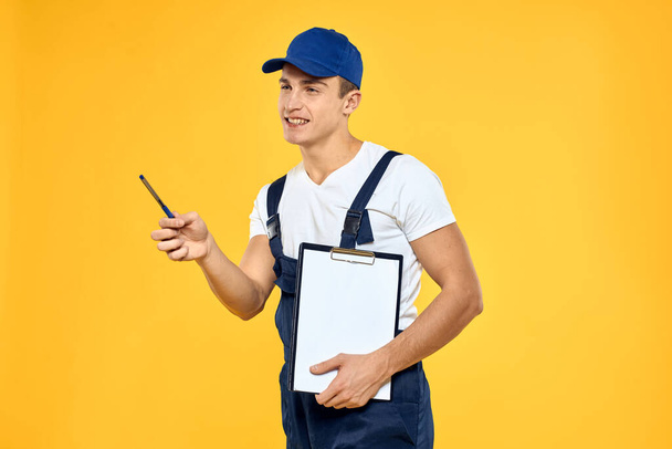 Man in working uniform documents rendering of services delivery service yellow background - 写真・画像