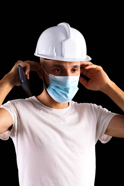 Young hispanic male construction worker putting on a mask - Foto, afbeelding
