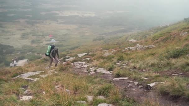 man reiziger draagt een toeristische rugzak op zijn schouders klimt de berg op - Video