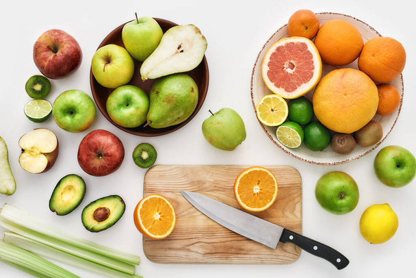 Top view of various colorful fresh summer fruits, Sliced fruits and a knife on cutting board isolated over white background - Photo, image