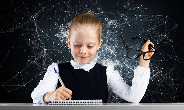 Smiling little girl in schoolwear doing homework - Foto, immagini