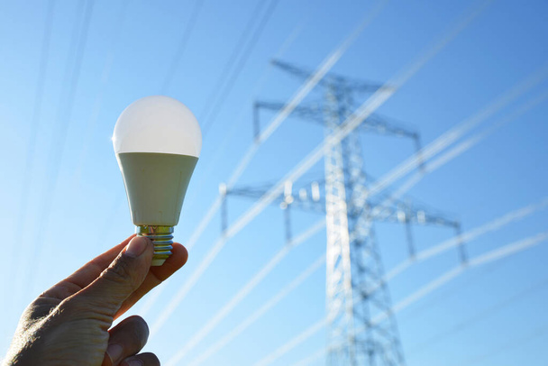 Hand holding eco LED light bulb with transmission tower at the background. Energy saving concept. - Photo, Image