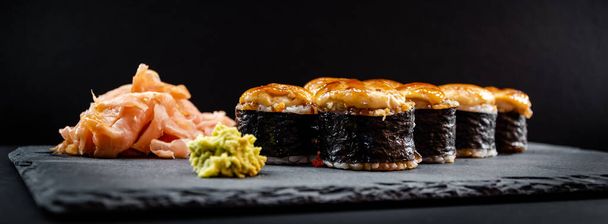 Photo panoramique de sushis chauds servis roulés en feuilles nori avec gingembre et wasabi sur une plaque de pierre noire. - Photo, image