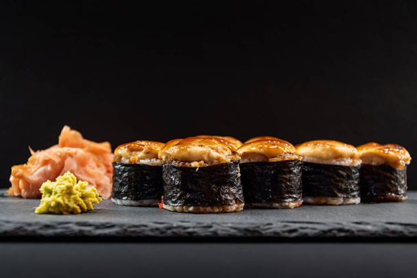 Sushis chauds servis roulés en feuilles nori avec gingembre et wasabi sur une plaque de pierre noire. - Photo, image