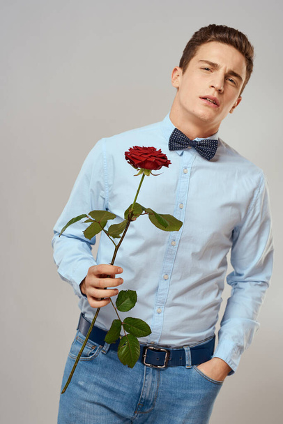 Handsome man with red rose blue shirt bow tie light background cropped view - Фото, изображение
