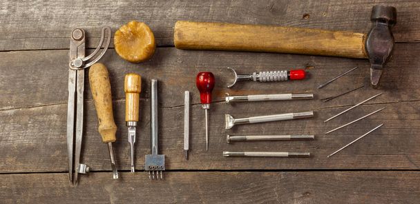 Set plano de kit de herramientas de cuero para principiantes. Antiguo instrumento retro para cuero que trabaja sobre fondo de madera. Panorámica. - Foto, imagen