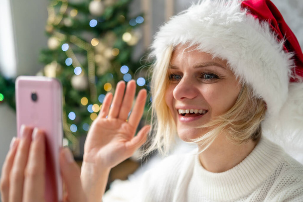 Christmas online congratulations. Smiling woman using mobile phone for video call friends and parents - Foto, immagini