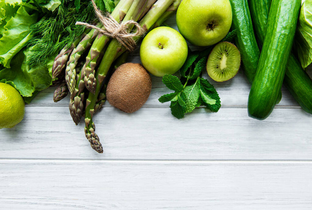 Gezonde vegetarische voeding concept achtergrond, verse groene voeding selectie voor detox dieet, appel, komkommer, asperges, avocado, limoen, salade bovenaanzicht op een witte houten achtergrond - Foto, afbeelding
