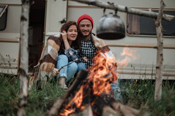 Paar in een geruite ruitjes roosteren marshmallows in brand in de buurt van de trailer huis - Foto, afbeelding