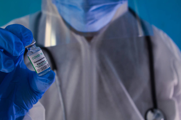 Arzt mit blauen Handschuhen, Maske, Brille, Stethoskop, in der Hand einen grünen Impfstoff Covid 19 Flasche. - Foto, Bild