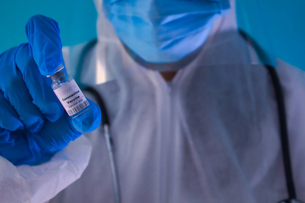 Orvos kék kesztyűvel, maszk, szemüveg, sztetoszkóp, kezében egy rózsaszín vakcina covid 19 palack. - Fotó, kép