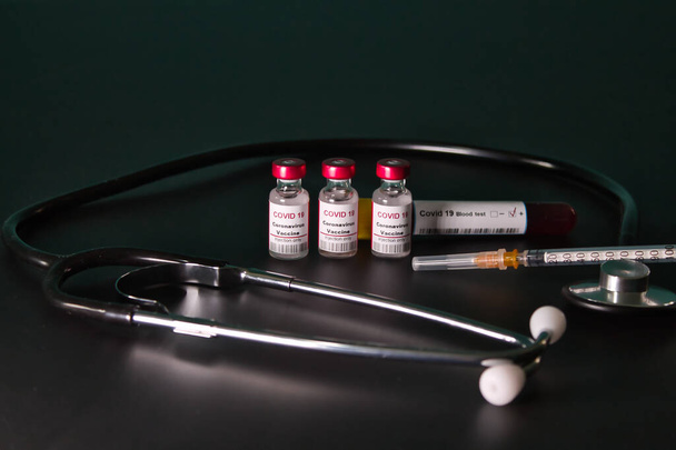 Stromově červené vakcíny covid 19 připravené k injekci a pozitivní krevní testy a pozitivní krevní testy na černém stole v laboratoři, obklopen stetoskopem a s injekční stříkačkou. - Fotografie, Obrázek