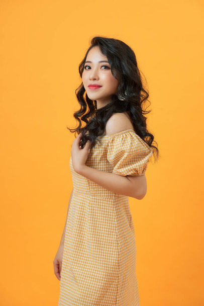 Portrait of a smiling attractive woman in summer dress posing while standing isolated over yellow background - Photo, Image