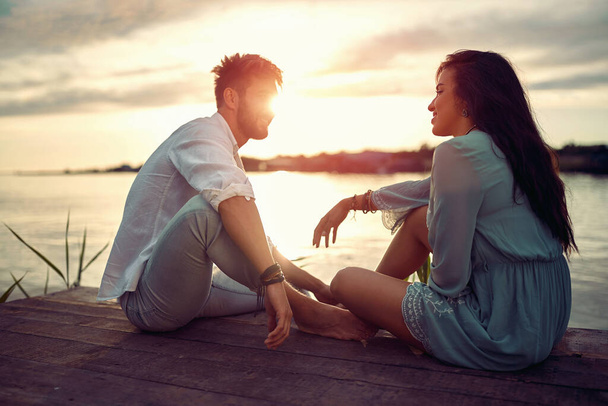 Young couple in love enjoying the sunset on the lake - 写真・画像