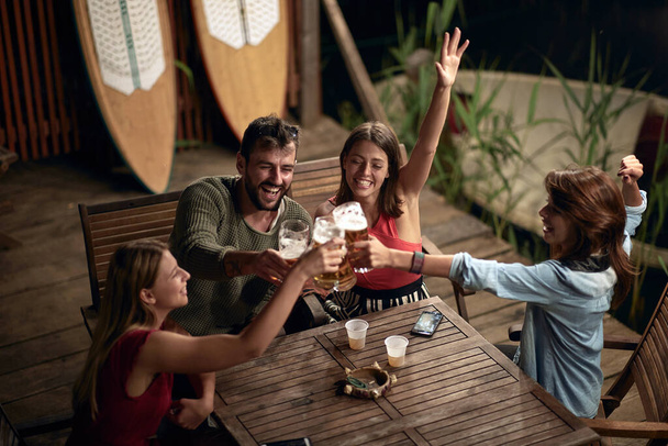 A cheerful company making a toast in the bar on the lake in a beautiful night - Фото, зображення