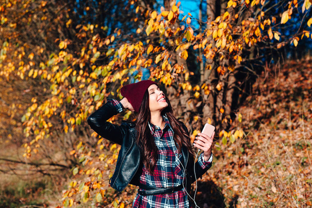 Young woman in plaid shirt listening to the music in autumn park - Foto, Imagem