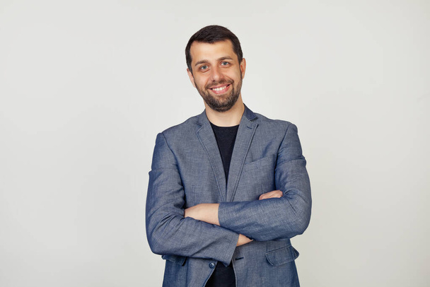 Young businessman with a smile man with a beard in a jacket, happy face, smiling with crossed arms, looking at the camera. A positive person. Portrait of a man on a gray background. - Foto, Imagem