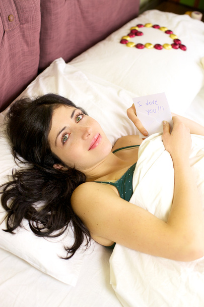 mooie vrouw in bed met liefdesbrief van vriendje - Foto, afbeelding
